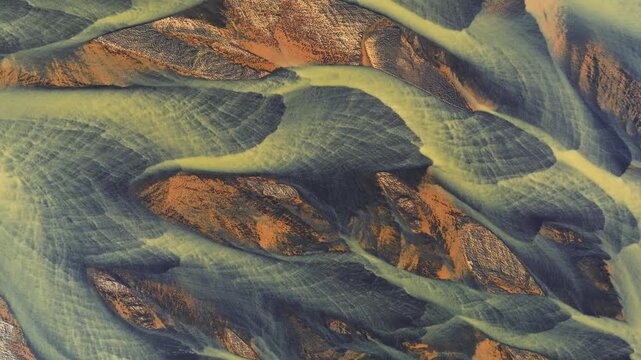 Aerial view of a braided river flowing through a landscape, the water creating intricate patterns around the rocky terrain, Grindavikurbaer, Iceland.