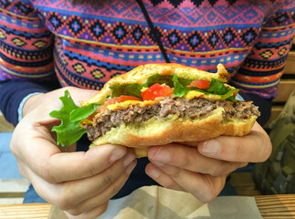 Manos sujetando una hamburguesa a medio comer. Hamburguesa con queso, tomate y lechuga mordida tras ser servida en un restaurante de Nueva York.