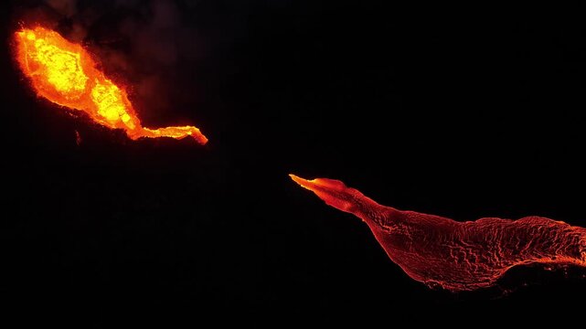 Aerial view of molten lava flows, with vivid orange and red hues contrasting against the dark landscape, creating a dramatic scene, Grindavikurbaer, Iceland.