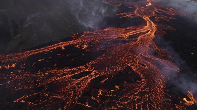 Aerial view of molten lava flowing through dark volcanic terrain, creating a dramatic contrast between the glowing orange lava and the black surroundings, Reykjanes, Grindavikurbaer, Iceland.