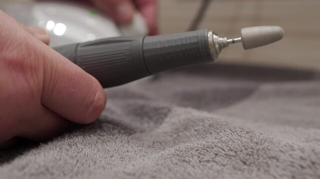 A metal and plastic electric manicure drill is turned off. The motor's humming whir slows, its pitch decreasing until the rotation stops completely.