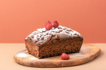Chocolate loaf cake with raspberries and sugar powder on brown background. Closeup