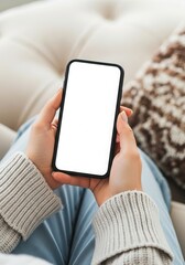 Woman holding a smartphone with a blank white screen while relaxing on a couch in a cozy home setting perfect for app promotion or mobile technology advertising