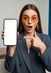 Stylish woman with orange glasses presenting a blank smartphone screen with a surprised expression in a professional setting for advertising and marketing use