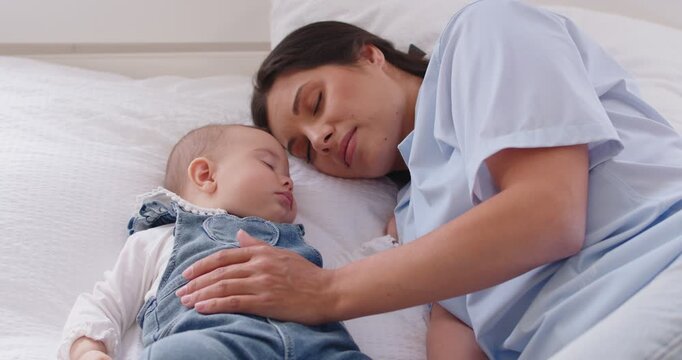 Calm relaxed little child and mother sleeping together in bed, having day nap at home, enjoying tranquil atmosphere, having healthy sleep. Baby and mom watching sweet dreams in bedroom