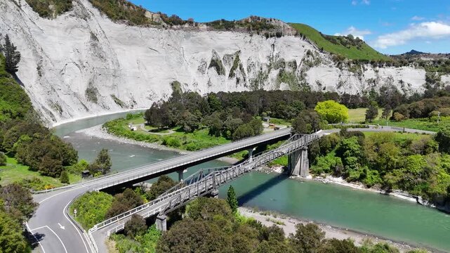 Aerial view of two bridges crossing the Rangitikei river, contrasted against the backdrop of rugged cliffs and lush greenery, Mangaweka, Manawatu-Whanganui Region, New Zealand.