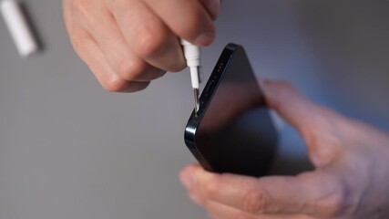 Closeup of hands cleaning smartphone case with precise tool, performing essential maintenance for digital device care and extending gadget lifespan at workshop. Concept of cellphone service.