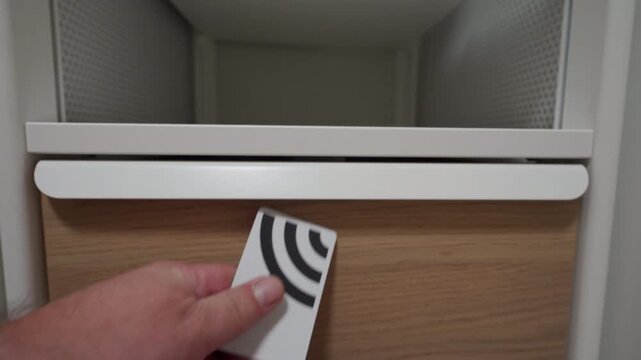A hand inserts a plastic key card into the slot of a modern electronic lock on a wooden locker or drawer. The lock mechanism makes a short, distinct buzzing sound as it actuates to unlock