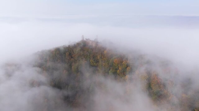 Aerial view of Auerbach Castle ruins atop a hill shrouded in swirling fog, creating a misty and ethereal landscape, Bensheim, Hessen, Germany.