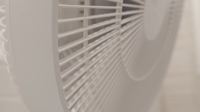 A white plastic floor fan has its settings adjusted. Switching between different modes or speeds is confirmed by a series of short, distinct electronic beeps, while the fan blades continue to whir