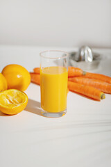Fresh carrot orange juice in a glass on a white table.