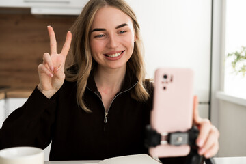 Young woman showing victory gesture sitting at table in the kitchen