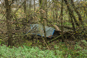 an old tarpaulin as a roof for a homeless person's sleeping place in the forest in autumn