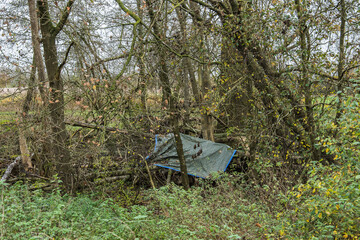 an old tarpaulin as a roof for a homeless person's sleeping place in the forest in autumn