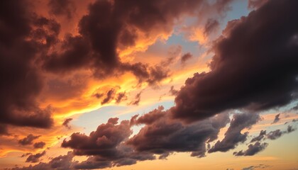 Dramatic sky with dark, heavy clouds illuminated by a vibrant orange and yellow sunset, creating a dynamic and atmospheric scene.