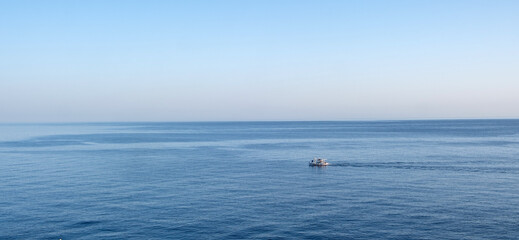 Small fishing boat crossing calm blue ocean water under clear sky image