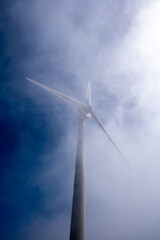 Wind turbine mast emerging through soft misty fog, viewed from below against bright sky image