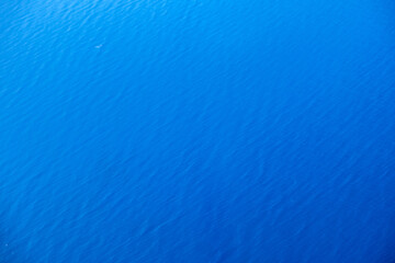 Minimalist aerial view of tranquil blue water surface featuring gentle ripples within bright daylight