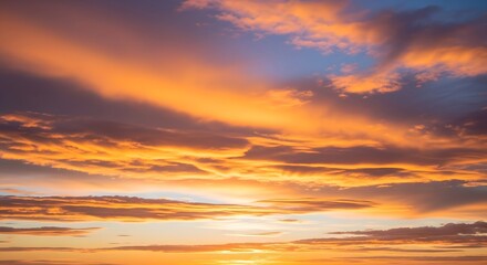 Fototapeta premium Warm golden and orange clouds stretched across a glowing sunset sky, blending softly with hints of blue to create a peaceful, radiant horizon.