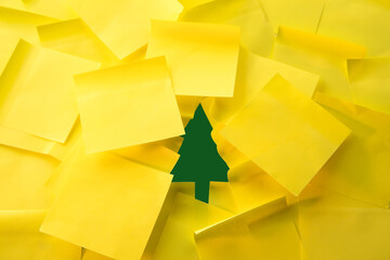 Christmas tree cutout hidden behind yellow sticky notes, green paper Christmas tree is partially revealed beneath layers of yellow post-it notes, office-themed seasonal campaign, holiday concept