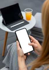 Woman using smartphone with blank screen next to tablet and orange juice on a modern table for mockup and lifestyle content creation and digital marketing