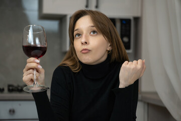 Young woman wearing a black turtleneck is savoring a glass of red wine in a contemporary kitchen, her thoughtful expression suggesting contemplation of its flavor and aroma