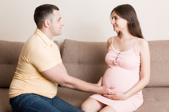 A young couple is expecting a baby. husband hugs the belly of his pregnant wife at home