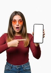 Surprised woman with orange glasses pointing at a blank smartphone screen against a white background showcasing a modern mobile device display