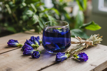 Butterfly pea flower tea in glass on wooden table with petals