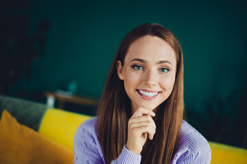 Young smiling brunette woman in pastel sweater sitting on a sofa at home with colorful cushions in a cozy living room