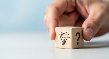 Hand holding a wooden cube with a light bulb symbol and a question mark, representing ideas and solutions