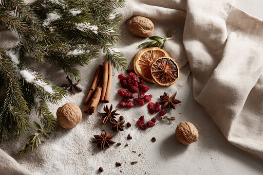 Flat lay of winter spices: star anise, cinnamon sticks, cloves, dried orange slices, cranberries, walnuts, all arranged on natural linen