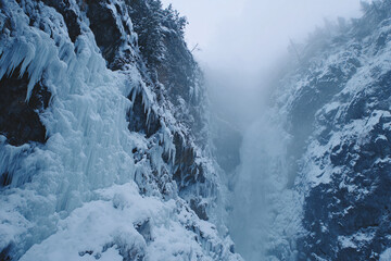 Frozen waterfall with icicle formations, blue-white winter tones, misty cold atmosphere, cinematic nature scene