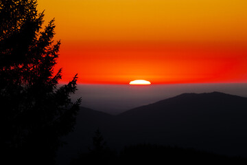 Half-set sun glows over rolling peaks, bathing the sky in molten reds and oranges. A dark pine silhouette anchors the scene, creating a serene landscape ideal for travel, wellness, and branding.!