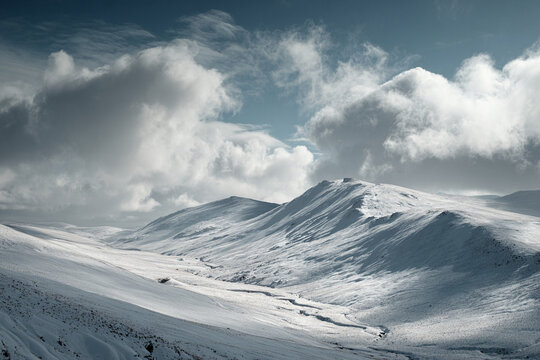 Rolling winter hills covered in wind-shaped snow patterns, dramatic clouds above, natural minimalism, ultra sharp details