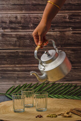 A person is pouring tea into three cups. The cups are on a wooden table.