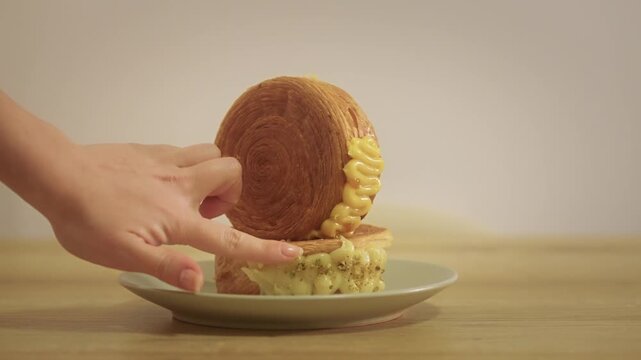 Slow motion close-up of a hand picking up a New York roll pastry from a plate, showing flaky layers and cream filling