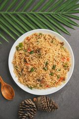 A bowl of fried rice with vegetables and meat on a wooden table.