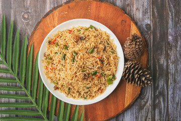 A bowl of fried rice with vegetables and meat on a wooden table.