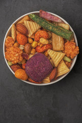 A bowl of assorted snacks including nuts, raisins, and potato chips.