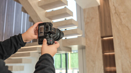 Photographer holding a camera, capturing a modern interior with a staircase © shine.graphics