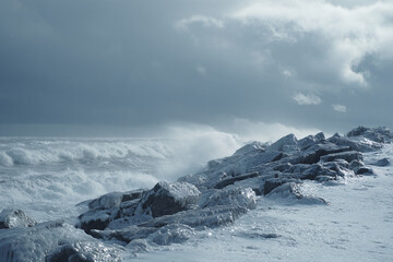 Strong waves hitting icy rocks, grey dramatic sky, winter ocean power, ultra realistic textures