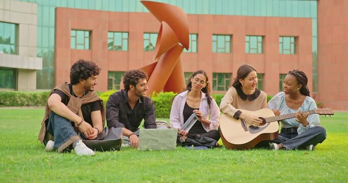 Indian young adult gen z female woman hold guitar play music man male group sing new song sitting garden park Happy relax girl boy team guy spend break time mood have fun joy enjoy new day place