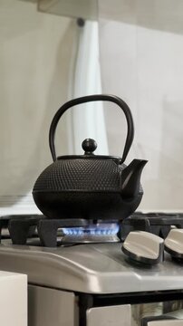 Iron teapot heating on a stovetop with hot tea inside, steam rising gently as the camera moves in a smooth tilt shot.