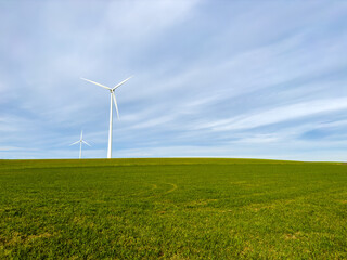 Minimal landscape with three wind turbines on a grassy ridge under soft blue sky