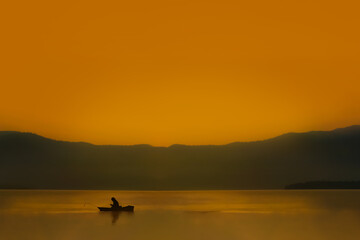 Silhouette fishing man sit in his boat and looking smart phone with sunrise sky and selective focus. Background for weekend hobbies, travel business, recreation and relaxation after working hard.