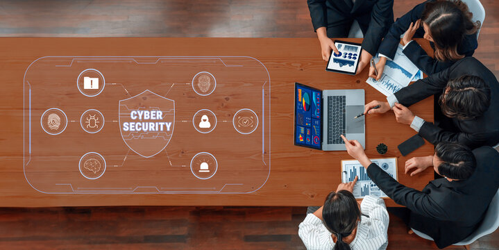 Professionals engage in a strategic meeting focused on cyber security, utilizing laptops and tablets while surrounded by digital data visuals and charts. Trope