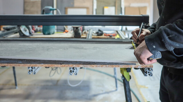 Craftsman measuring and marking a large tile for cutting in a workshop