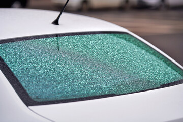 Rear car window coated with frost and tiny frozen droplets formed by freezing rain, low visibility and illustrating the challenges of driving in cold winter weather with icy surfaces. Selective focus
