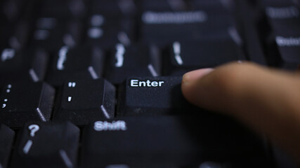 Finger pressing Enter key on black keyboard — typing, submit and technology concept (close-up)